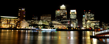 Canary wharf night This image is an urban landscape photograph taken at night, capturing the city architecture of Canary Wharf in London, United Kingdom. The brightly illuminated office buildings, including the prominent One Canada Square and HSBC Tower, rise against the dark sky, reflecting their lights across the calm surface of the River Thames in the foreground. The scene was captured in early autumn, as suggested by the date, with the well-known skyscrapers of London showcasing a modern architectural skyline. The city lights create vivid reflections on the River Thames, highlighting the dynamic urban environment of London at night.